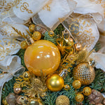 Decorative arrangement with gold ornaments and greenery, featuring a prominent yellow ornament.
