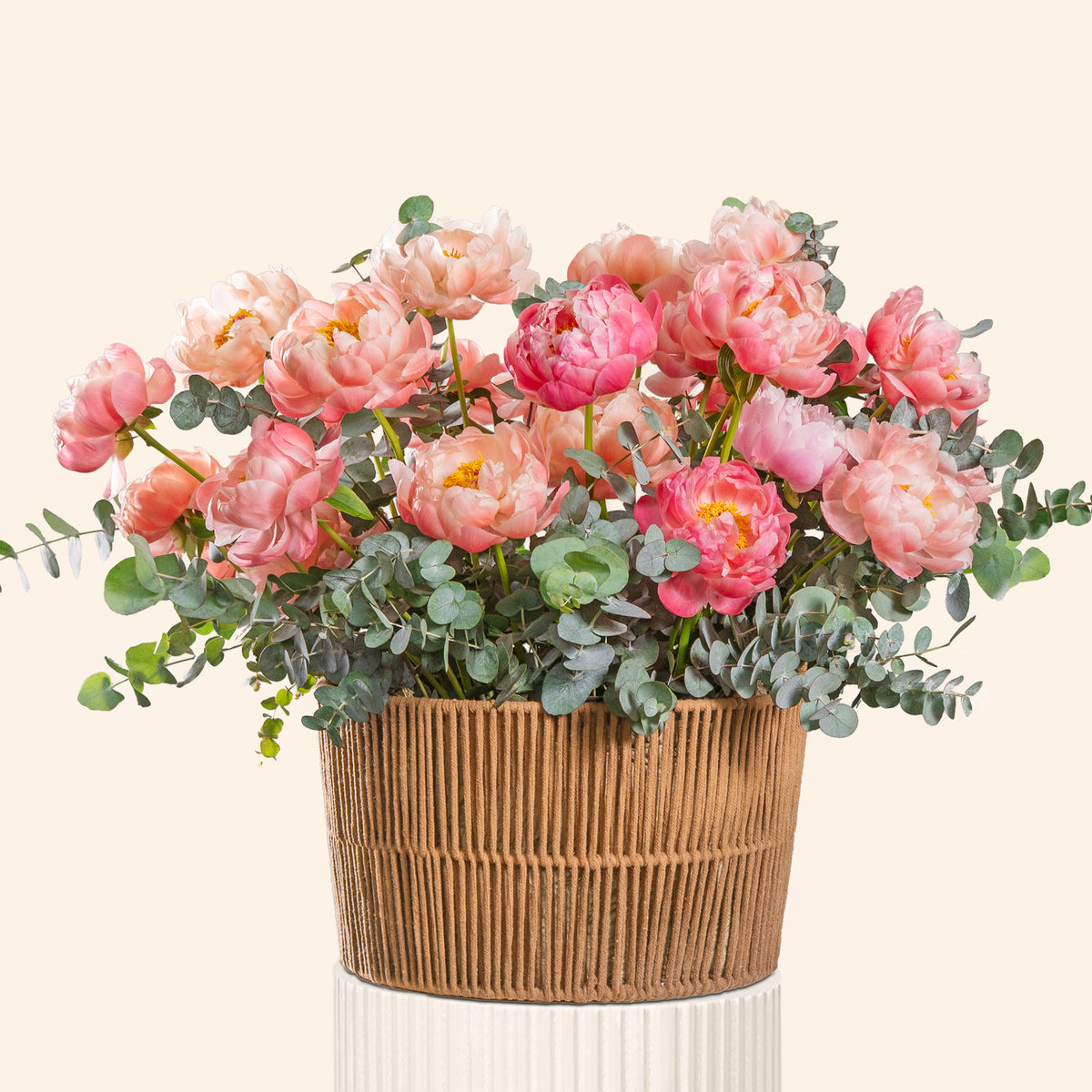 Bouquet of pink flowers in a woven basket on a light beige background