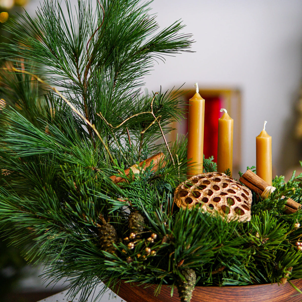 Decorative arrangement with greenery, candles, and a textured object in a wooden bowl.