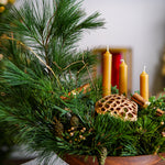 Decorative arrangement with greenery, candles, and a textured object in a wooden bowl.