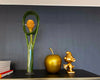 Decorative items including a green vase, gold apple, and gold figure on a shelf against a dark wall.