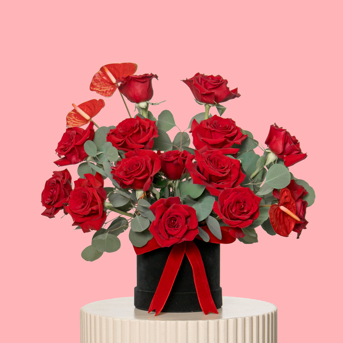 Bouquet of red roses with a black vase and red ribbon on a pink background
