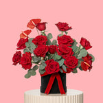Bouquet of red roses with a black vase and red ribbon on a pink background