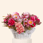 Bouquet of pink and red flowers in a white basket on a light beige background