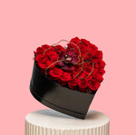 Heart-shaped black box filled with red roses on a pink background