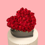 Heart-shaped arrangement of red roses on a white stand with a pink background