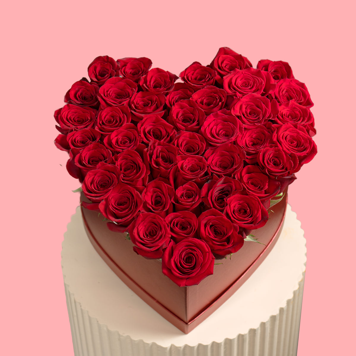Heart-shaped box of red roses on a white cake with a pink background