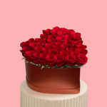 Heart-shaped box filled with red roses on a pink background
