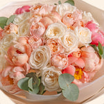 Bouquet of pink and white flowers with green leaves in a white container.
