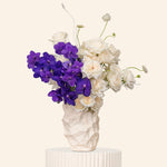 Floral arrangement with purple and white flowers in a textured vase on a light background