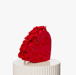 Red heart-shaped bag with floral details on a white pedestal against a white background