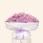 Bouquet of purple flowers in a white container with a purple ribbon on a light beige background