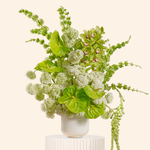 Decorative plant arrangement in a white vase on a light beige background