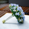 Bouquet of flowers with green leaves and white and blue flowers on a white surface.