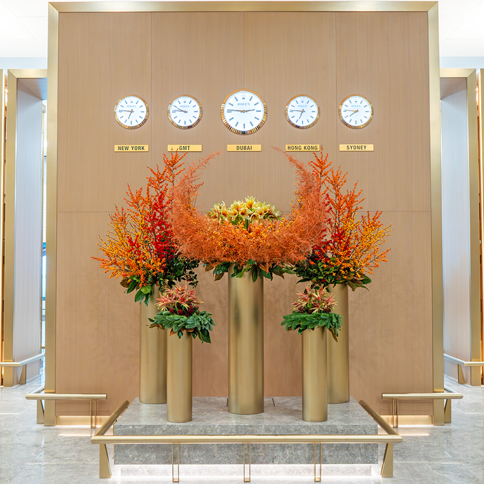 Decorative setup with floral arrangements in tall vases against a wall with clock faces and city names.