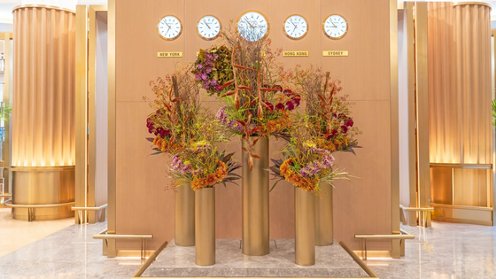 The Golden Ascent, a tall floral installation in Emirates First Class Lounge featuring Heliconia, Vanda orchids, spider chrysanthemums, and rosehips in golden and sunset tones, symbolizing Dubai’s ambition and luxury.