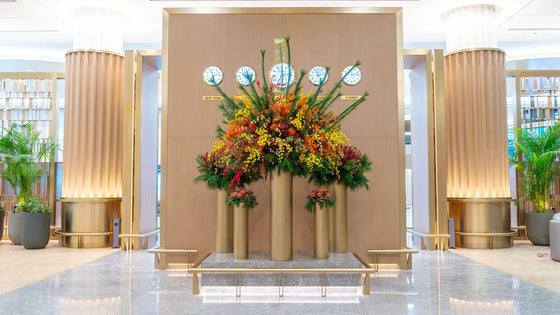Large autumn-inspired floral installation titled “Hortus Mundi,” featuring Proteas, orchids, Leucospermum, and Pinus Strobus arranged on tall gold columns inside a luxury Dubai lounge.