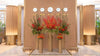 Large European Yuletide Vista floral installation in Emirates First Class Lounge featuring red Ilex, orange lilies, and winter greens arranged on gold pedestal vases.