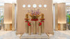 Decorative setup with floral arrangements in tall cylindrical vases against a beige wall with clock displays.