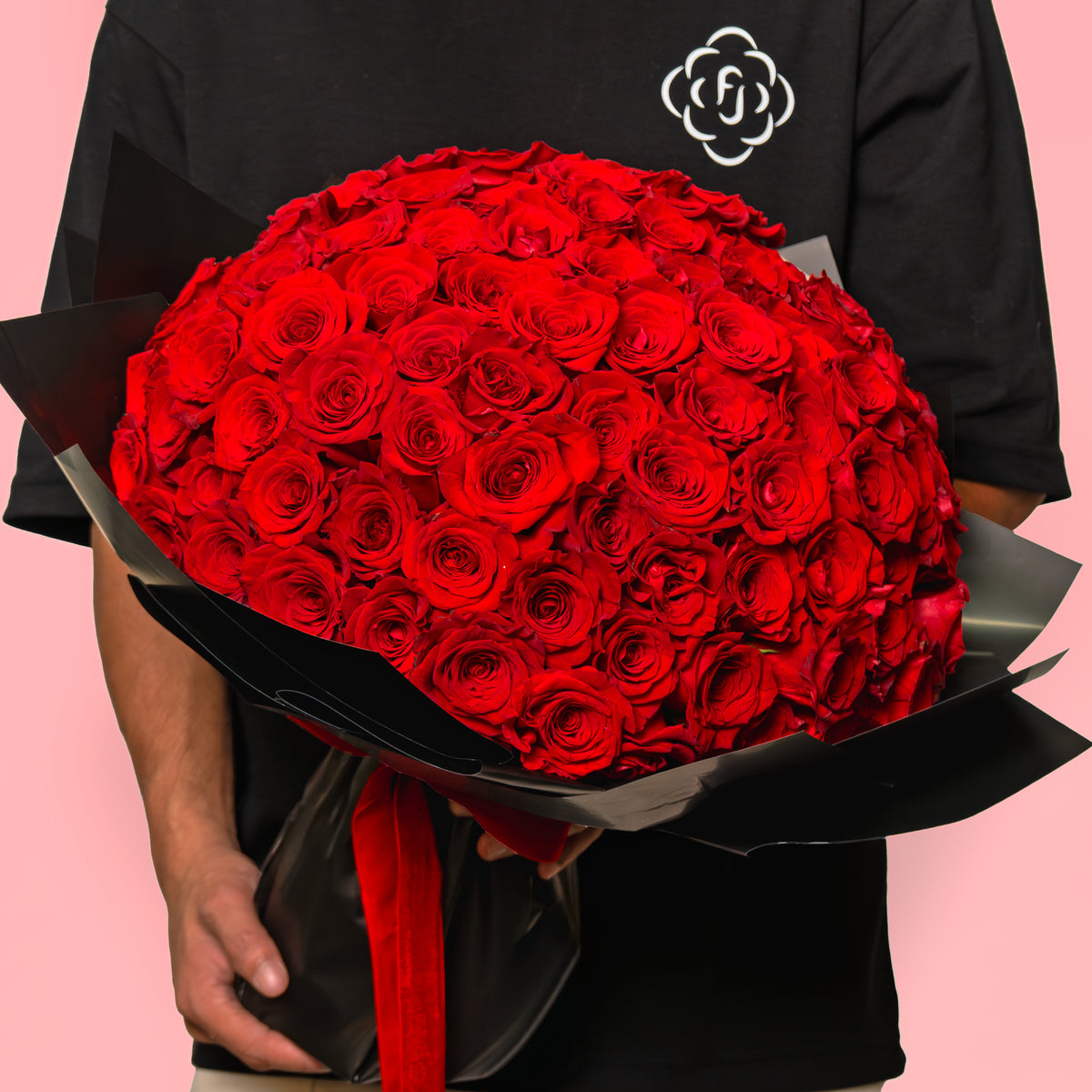 Bouquet of red roses held by a person against a pink background
