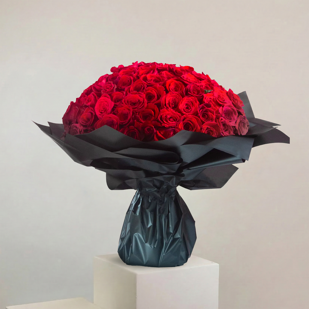 Bouquet of red roses wrapped in black paper on a white pedestal against a light gray background