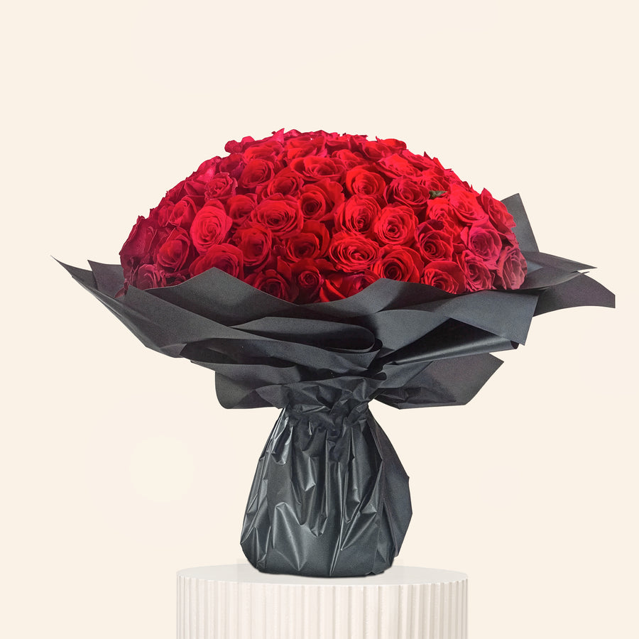 Bouquet of red roses wrapped in black paper on a white pedestal against a light gray background