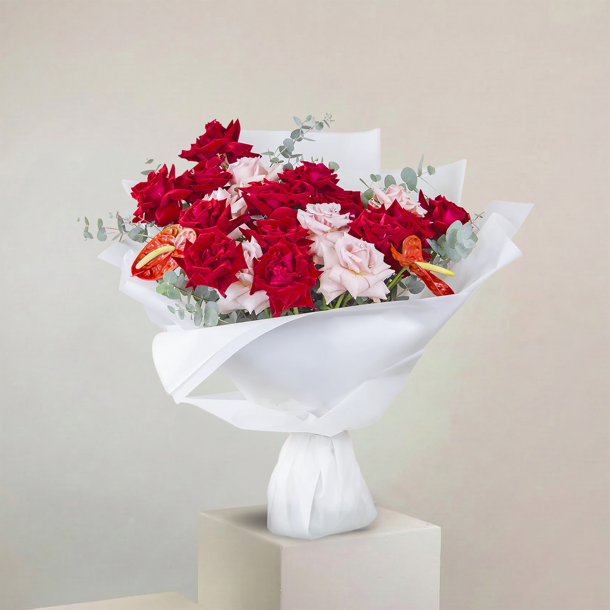 Bouquet of red and pink flowers on a white pedestal against a beige background