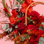 Basket of red roses with greenery on a pink background