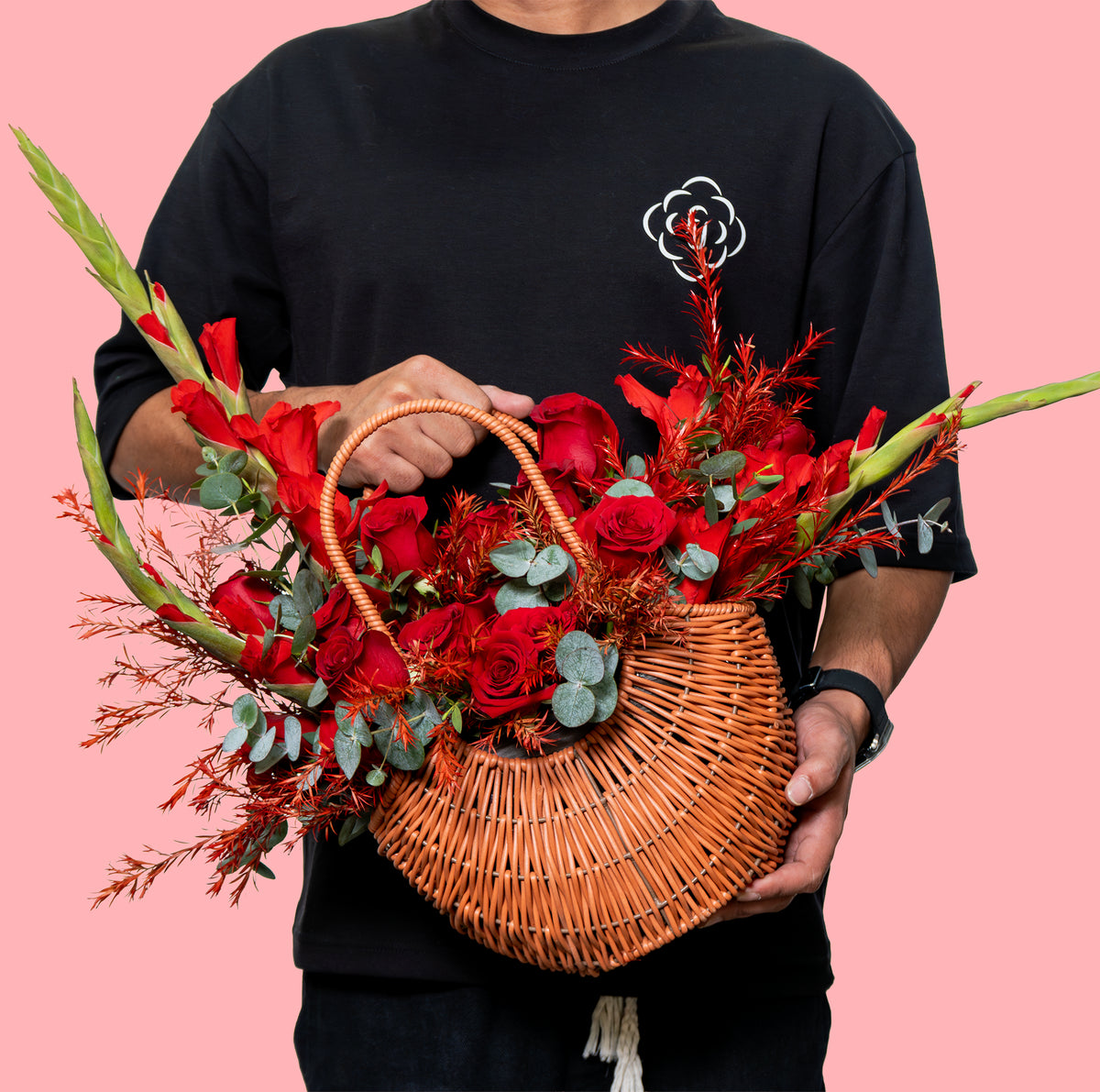 Person holding a woven basket filled with red flowers against a pink background
