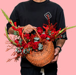 Person holding a woven basket filled with red flowers against a pink background