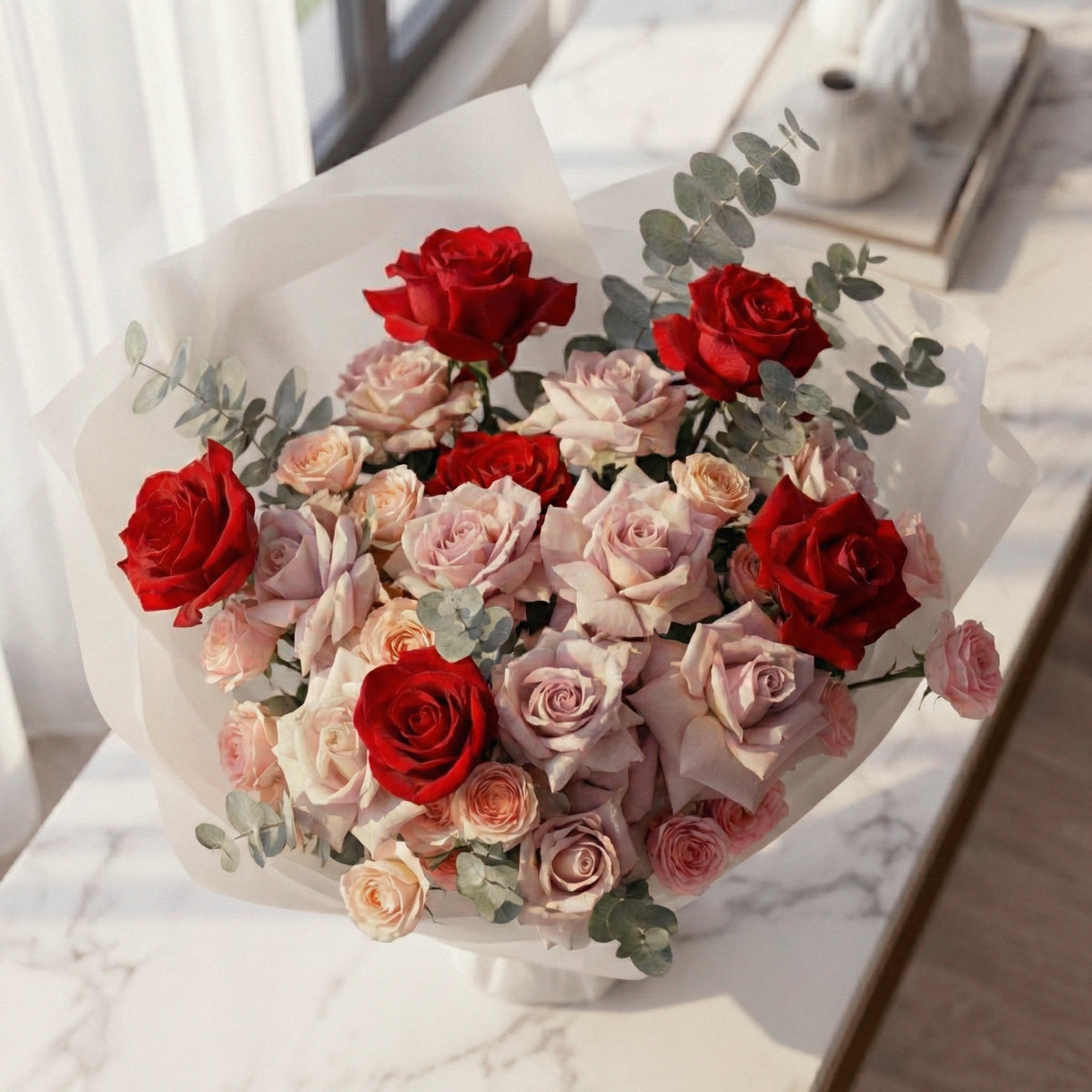 Bouquet of red and pink roses with greenery on a marble surface