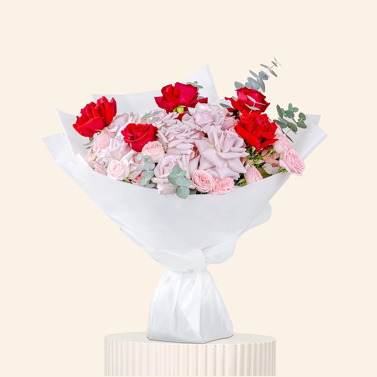 Bouquet of red and pink flowers wrapped in white paper on a light gray background