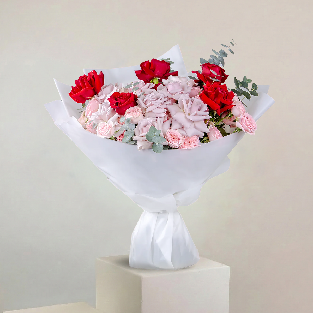 Bouquet of red and pink flowers wrapped in white paper on a light gray background