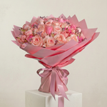 Bouquet of pink flowers wrapped in pink paper with a bow on a light background