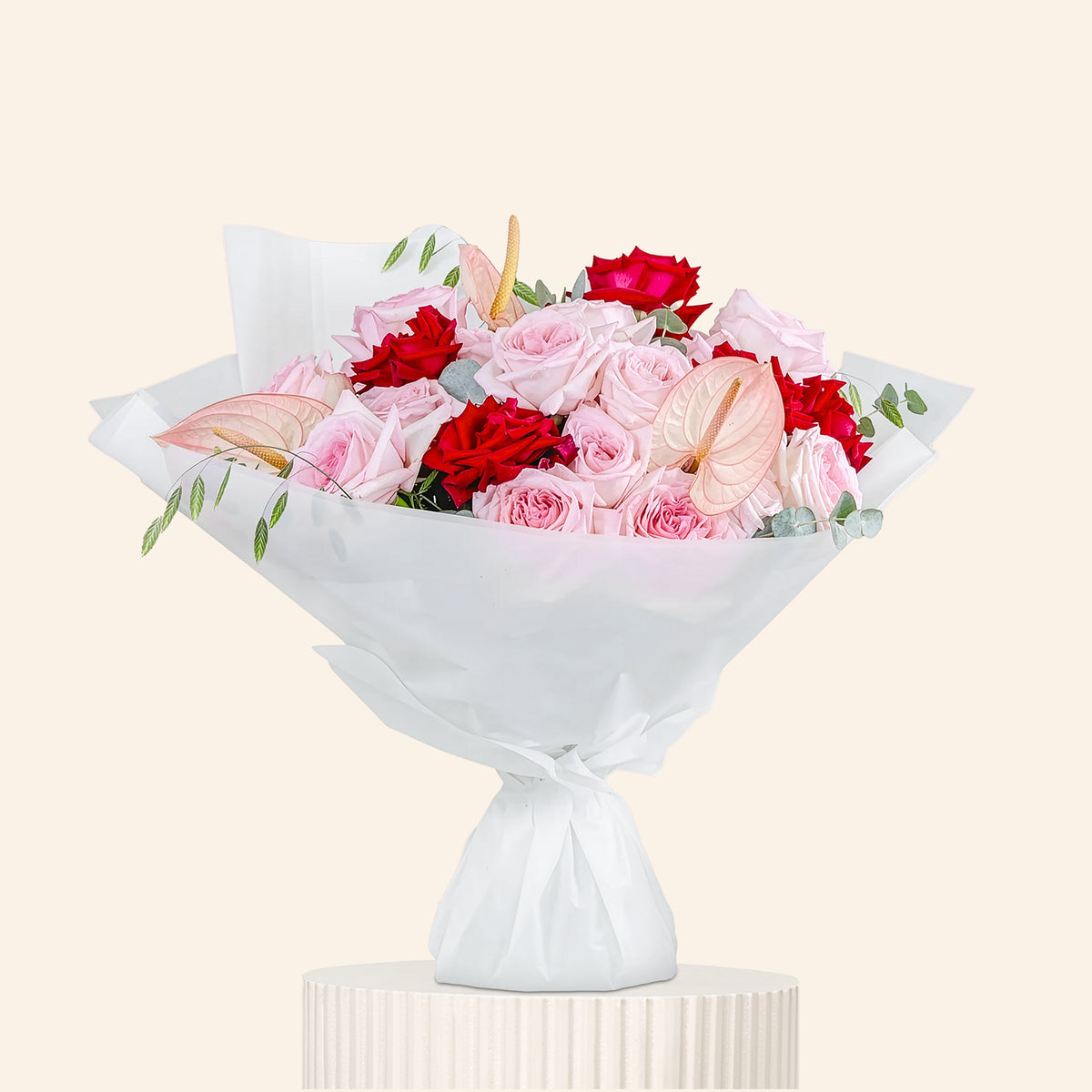 Bouquet of pink and red flowers wrapped in white paper on a beige background
