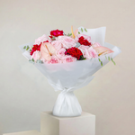 Bouquet of pink and red flowers wrapped in white paper on a beige background
