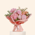 Bouquet of pink flowers with greenery on a white pedestal against a light beige background