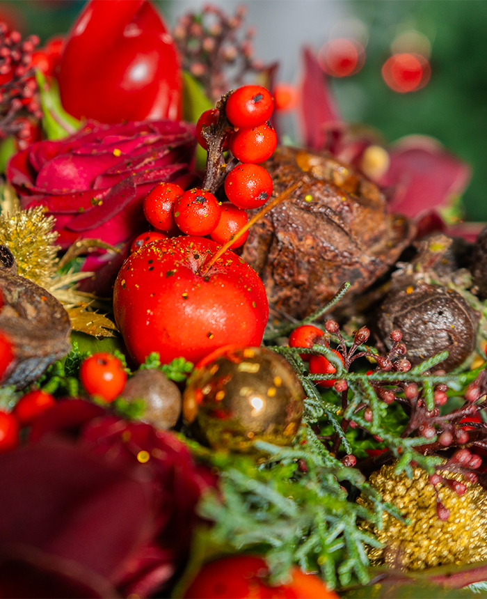 Close-up of a festive arrangement with red berries, gold ornaments, and greenery.