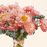 Bouquet of pink flowers with green leaves in a clear vase on a light background