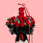Bouquet of red and black roses with a teddy bear on a pink background