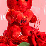 Red teddy bear with a heart and roses on a pink background