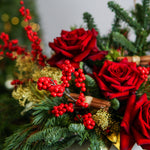 Decorative arrangement with red roses, red berries, and greenery on a blurred background