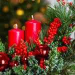Decorative arrangement with red candles, berries, and ornaments on a blurred Christmas tree background.