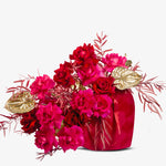 Bouquet of red and pink flowers with gold accents in a red vase on a white background