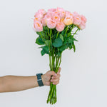 Hand holding a bouquet of pink roses against a light gray background