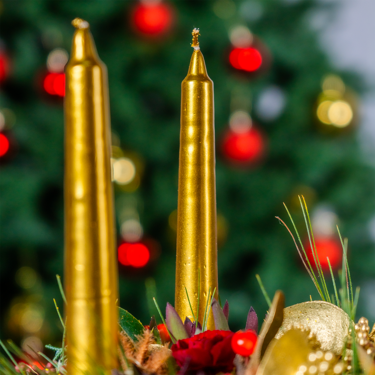 Two gold candles with a blurred Christmas tree in the background