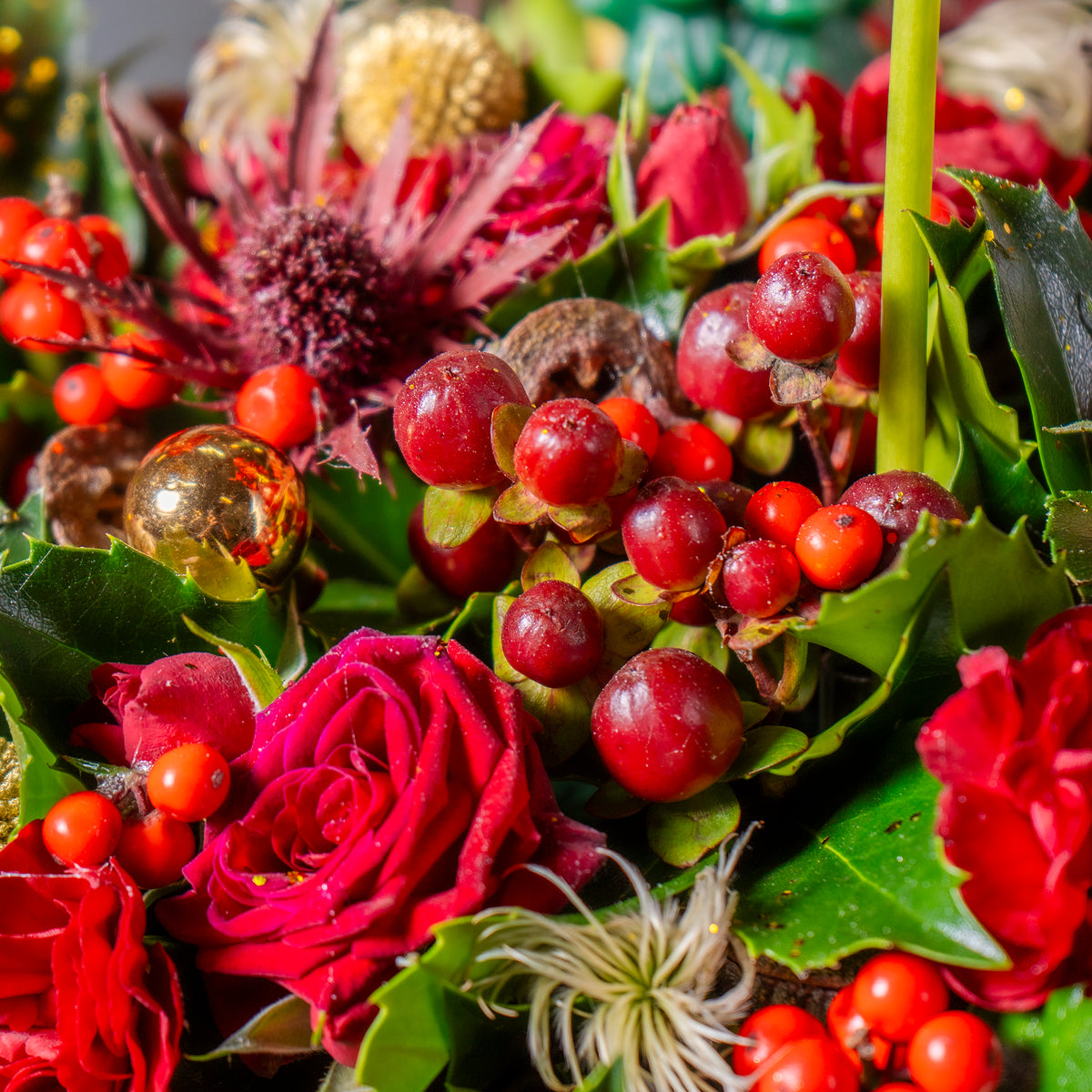 Close-up of a festive floral arrangement with red roses, berries, and greenery.