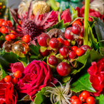 Close-up of a festive floral arrangement with red roses, berries, and greenery.