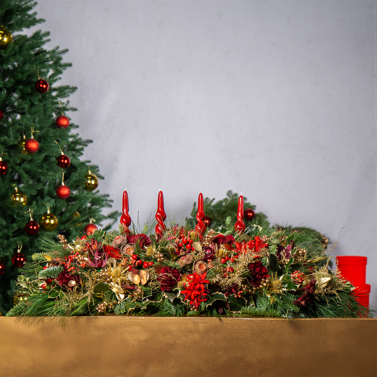 Decorative Christmas table setting with candles, flowers, and ornaments against a plain background.