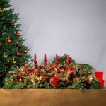 Decorative Christmas table setting with candles, flowers, and ornaments against a plain background.